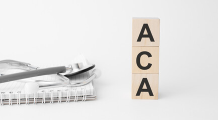 aca inscription on wooden cubes isolated on white background, medicine concept. Nearby on the table are a stethoscope and pills.