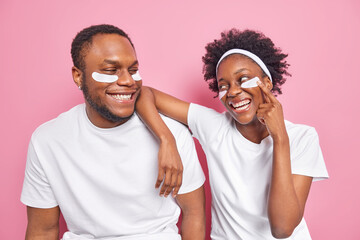 Indoor shot of happy carefree black woman and man looks with smile at each other apply beauty...