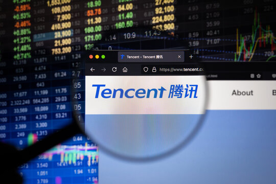 Tencent company logo on a website with blurry stock market developments in the background, seen on a computer screen through a magnifying glass