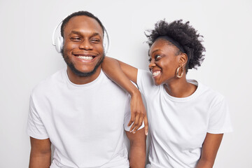Happy positive friendly Afro American teenage woman and man smile gladfully dressed in basic casual t shirts have good mood listen favorite music isolated over white background. Best friends ever