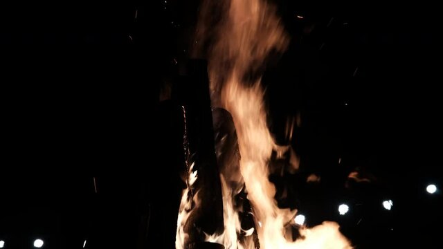 Big Bonfire Burns at Night on Nature in Slow Motion. Large Fire Flames on a Black Background. Fire sparks and flying embers in a dark. Raging campfire of wood. Real campfire from branches burns. 4K