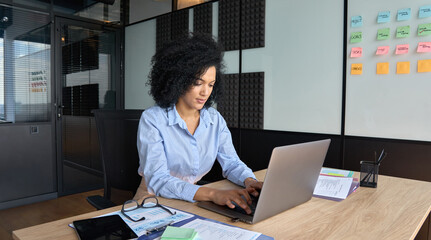 Young African American focused female ceo data analyst businesswoman sitting at desk working typing...