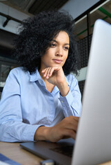 Young serious concerned African American businesswoman sitting at desk looking laptop computer in...