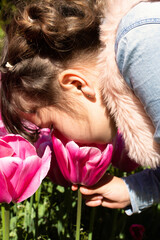 Naklejka premium Little girl poking her nose into an open pink tulip while holding it by the stem