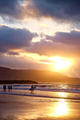 Sunset on the beach, surfers and swimmers in golden glow of the setting sun, las Canteras, Gran Canaria, Canary Islands.