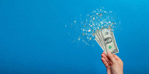Inflation, dollar hyper inflation. Banner with blue background. One dollar bill is sprayed in the hand of a man on a blue background. Price rise concept. - obrazy, fototapety, plakaty
