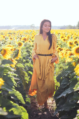 A brunette woman in a yellow dress on the field with sunflowers. Orange dress. Full length
