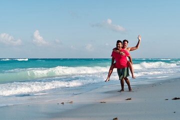 homosexual couple of two men playing piggybacking on the shore of cancun beach