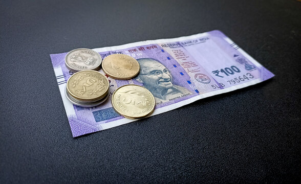 A Close up picture of a few Indian Coins and a hundred rupee banknote i;n  vibrant purple against a black background.