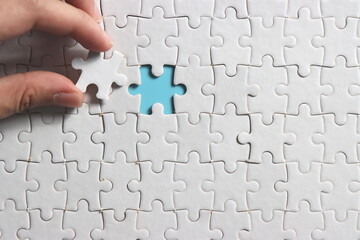 hand holding a piece of jigsaw puzzle to assemble complete the puzzle. selective focus.