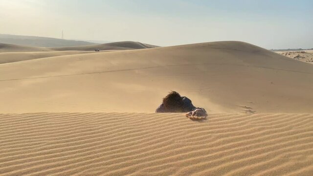 A man in an office cloth crawls up a dune in a desert. Overcoming challenges in business