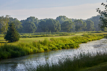 River running through green meadow and green trees during a beautiful summer day