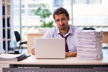 Fototapeta premium Young male employee unhappy with excessive work in the office