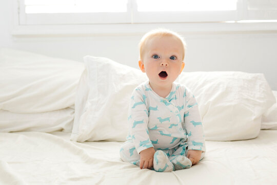 Baby boy with open mouth sitting on bed