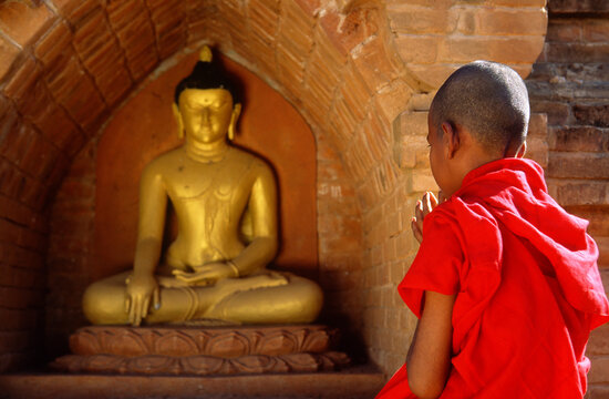 Myanmar, Mandalay, Novice monk praying in front of Buddha statue in temple
