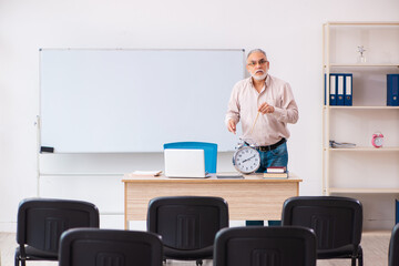 Old male teacher in the classroom in time management concept
