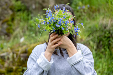 Fototapeta na wymiar The girl covers her face with a bouquet of wild forest flowers.
