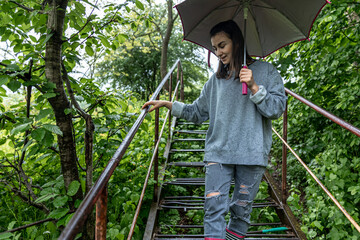 A girl walks in the forest with an umbrella in rainy weather.