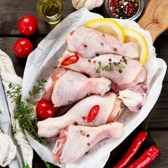 Raw chicken legs with spices and herbs for cooking on wooden background.
