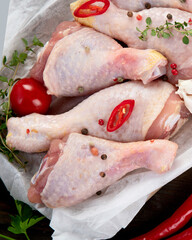 Raw chicken legs with spices and herbs for cooking on wooden background.