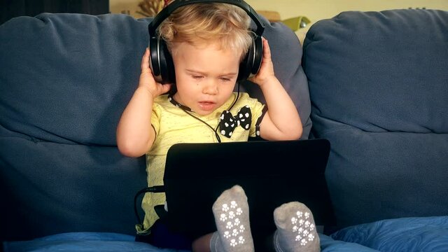 baby with tablet headphones on sofa. Smart media education. 4K