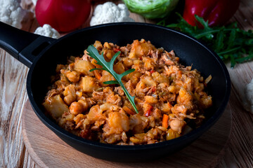 Homemade pork stew with vegetables, potato, onion, carrot, cauliflower, pepper with tomato sauce, garlic and herbs in a frying dish on wooden table.