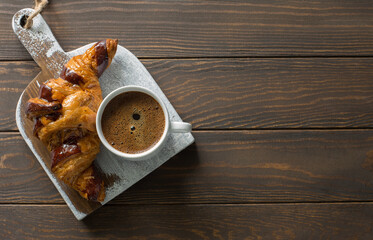 Croissant with  chocolate and cup of coffee on grunge cutting board close up