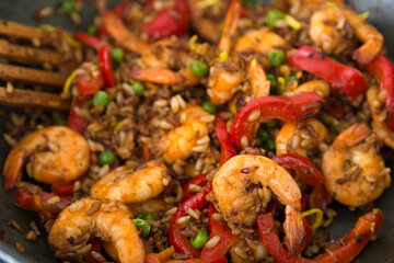 Chinese and Taiwanese homemade street food travel concept. Braised shrimp over fried rice with assorted vegetables for asian or indian lunch menu on the black pan with red peppers and green peace