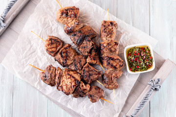 Grilled sirloin tips or beef meat skewers with chimichurri sauce, on wooden tray, horizontal, top...