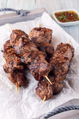 Grilled sirloin tips or beef meat skewers with chimichurri sauce, on wooden tray, vertical