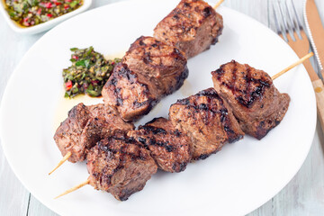 Beef meat skewers with chimichurri sauce, on white plate, horizontal