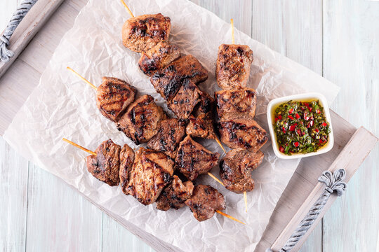 Grilled sirloin tips or beef meat skewers with chimichurri sauce, on wooden tray, horizontal, top view