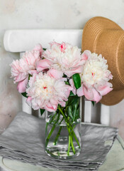 Cozy rustic still life - bouquet of pink peonies, a straw hat on a vintage wooden chair