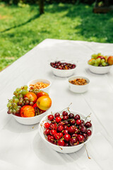 stylish vertical food content. ripe cherry berry, ripe juicy apples, grapes and nuts in white paper plates on light table in an open space green grass. healthy summer raw snacks. selective focus