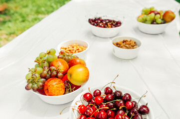 ripe juicy fruits: apples, grapes, cherries and nuts in white paper plates on a light table in an open space. healthy summer raw snacks for a party. healthy lifestyle. selective fous