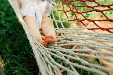 baby's feet, cute little heels in the grass and mud. an unrecognizable child lies on a hammock in the shade on a hot day. cute childhood moments. selective focus