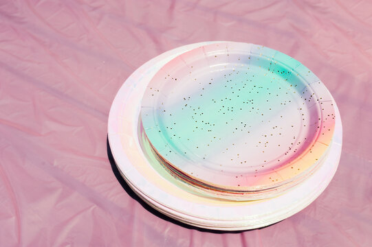 eco paper pink and rainbow tableware plates on dusty pink table and background bright green grass on sunny day. childrenparty in backyard. cartering. pink table setting. selective focus