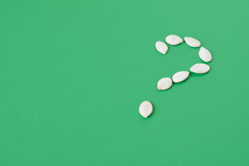 unpeeled pumpkin seeds laid out in the shape of a question mark on a green background