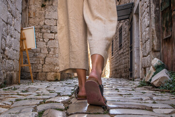 Detail shot of female legs wearing comfortable travel sandals walking on old medieval cobblestones...