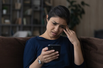 How is it. Confused indian female teenager sit on couch at living room seeing important call missed...