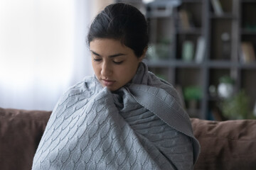 So cold. Young indian woman wrap up in blanket freeze at home feel ague shiver because climate...