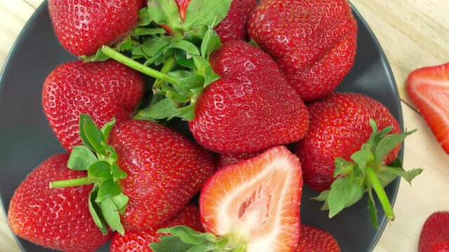 Top view Rotate Red Strawberries in a black bowl on wooden table, Fresh long stem berries, Organic Strawberry in Bamboo basket.