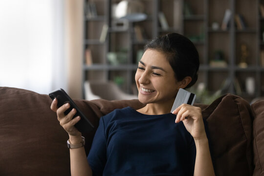 Home Shopping. Happy Millennial Indian Woman Sitting On Cozy Sofa Succeeded In Making Payment At Trusted Ecommerce Internet Site. Glad Young Lady Shopper Spend Money From Bank Card At Online Web Store