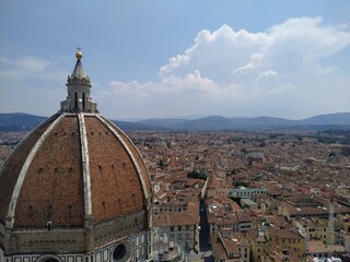 Fototapeta premium Die roten Dächer von Florenz mit Blick auf die Hügel im Hintergrund. Im Vordergrund ist die Kuppel des Doms zu sehen.