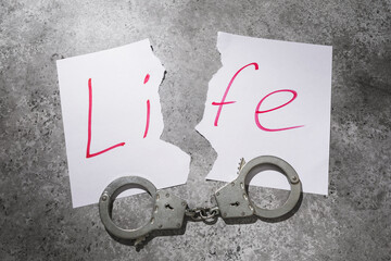 Torn sheet with text and handcuffs on the table, concept on the theme of a spoiled life