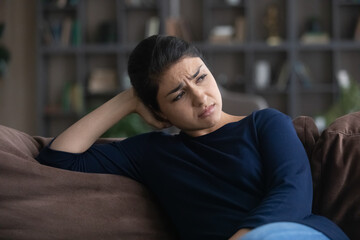 Melancholic mood. Sad depressed young indian woman sit on sofa at home alone think on love work...