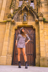 Street Style in the city, brunette Caucasian girl with gray dress and a beret, next to a cathedral in a photo pose, lifestyle of a model in the city, vertical photo