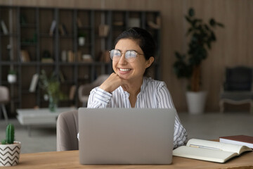 Young indian lady scientist in glasses work on pc do research sit by desk at home in library think of success distracted from screen. Teen female student relax from studying visualize good exam result