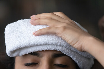 Wet compress. Close up cropped shot of sick young female having fever headache holding wet towel on...