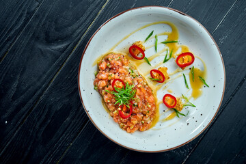 Delicious appetizer - salmon tartare with avocado and hot chilie pepper on a white plate on black wooden background.